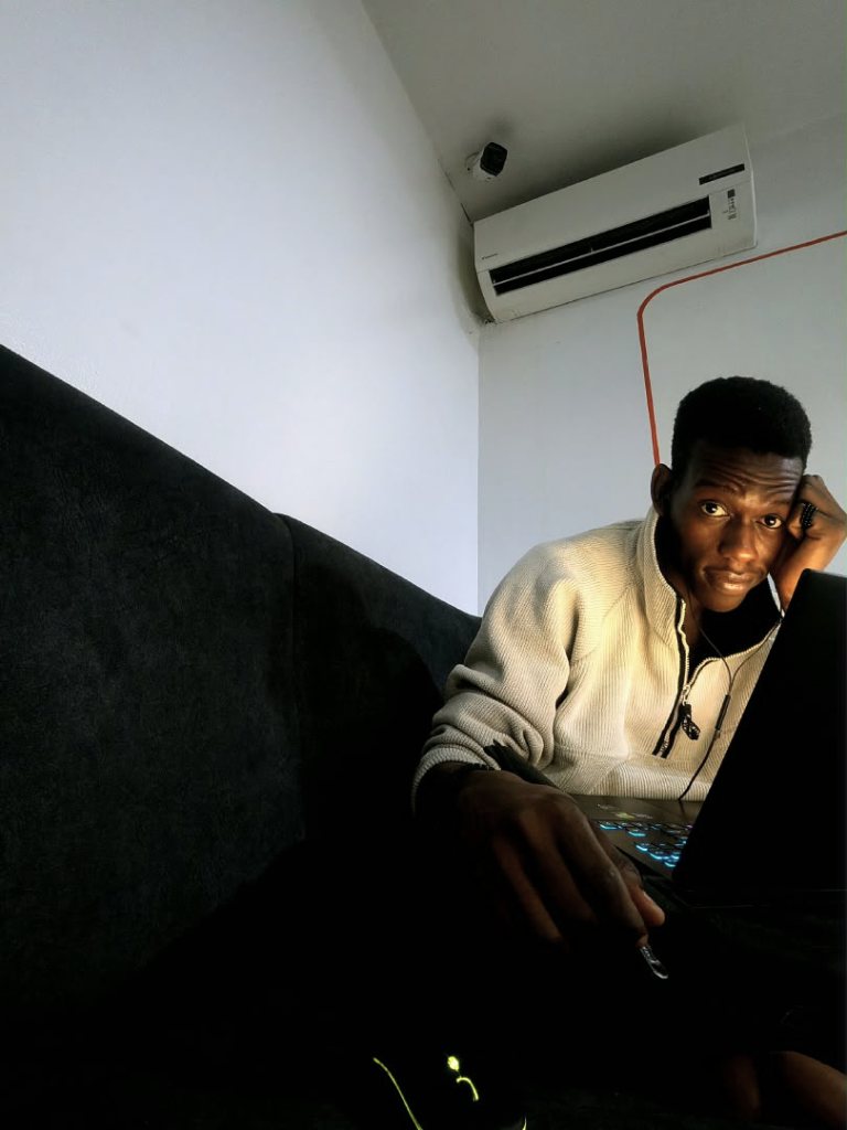 Ayobami at a laptop in a small office, one hand at his ear